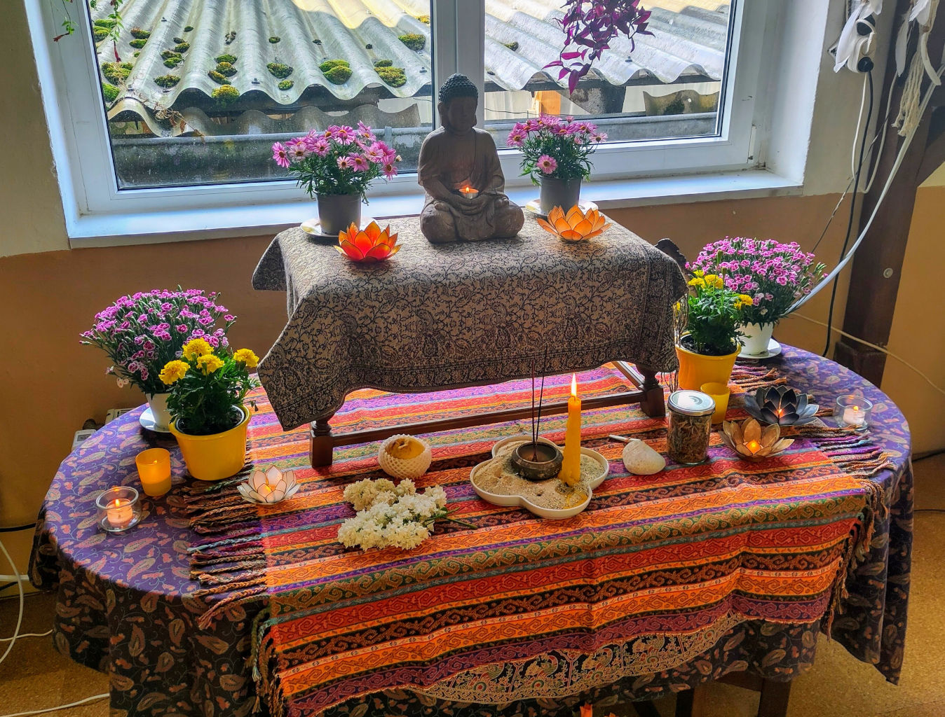 Buddhistischer Altar mit Buddhafigur, Kerzen, Blumen, Räucherstäbchen und Opfergaben während einer Puja.